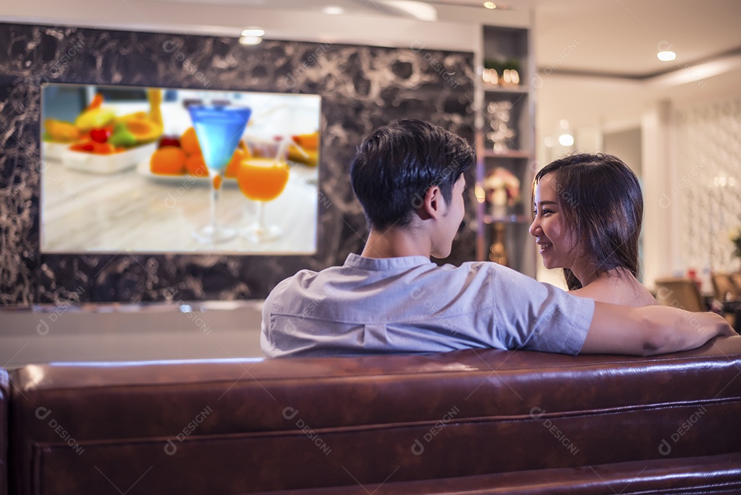 Amantes se olhando enquanto assistem televisão no sofá. Conceito de casal e relaxamento. Tema de lua de mel noturno, Vista traseira.