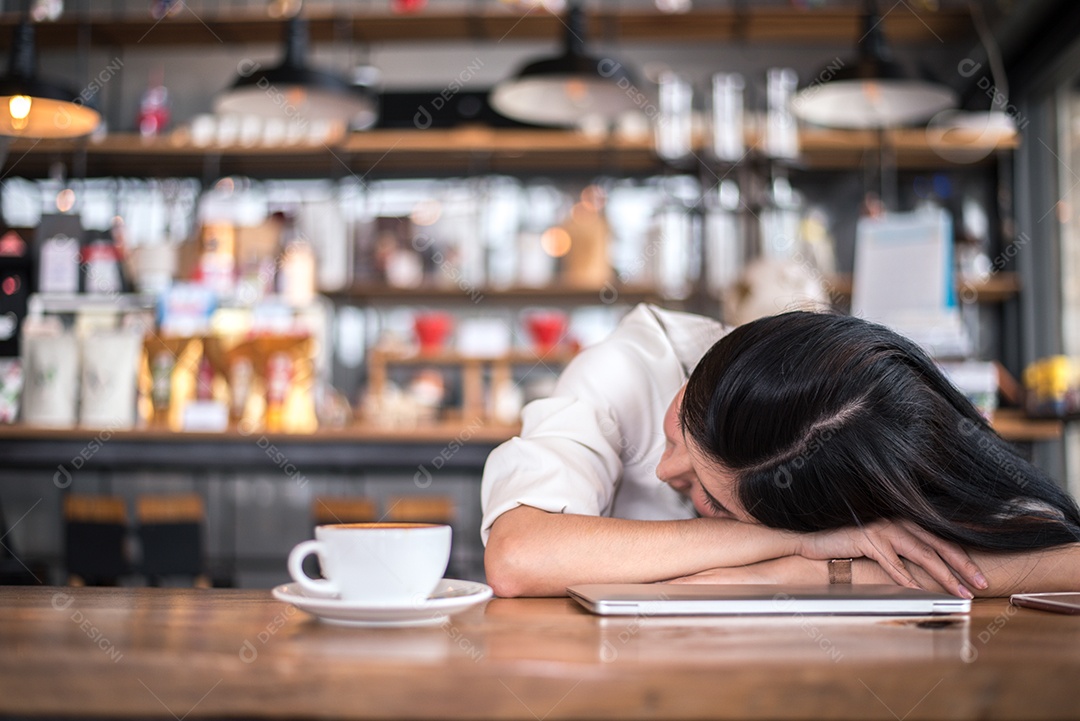 A mulher asiática está descansando e dormindo em uma cafeteria porque está cansada de trabalhar a noite toda.