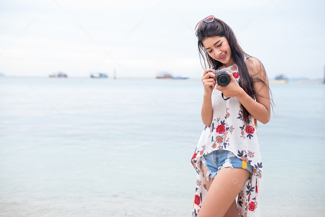 Mulher asiática gosta de tirar foto com câmera digital na praia. Conceito de mulher solteira e solitária.