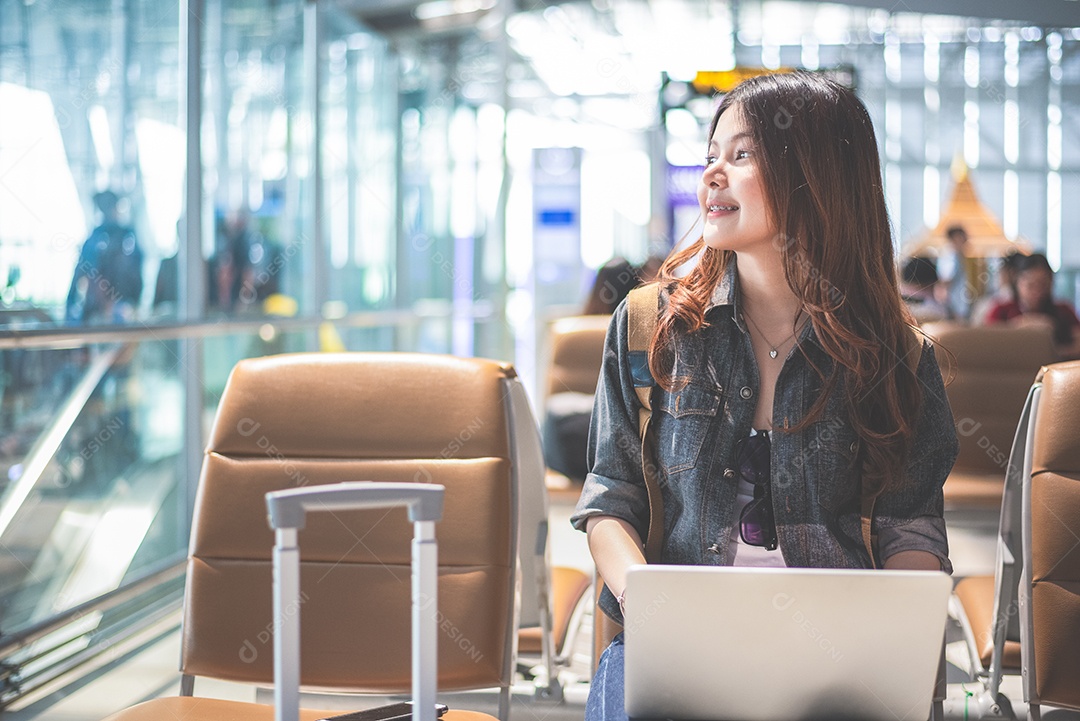 Mulher asiática de beleza usando laptop e olhando para fora no aeroporto. Mulher sentada no terminal do aeroporto.