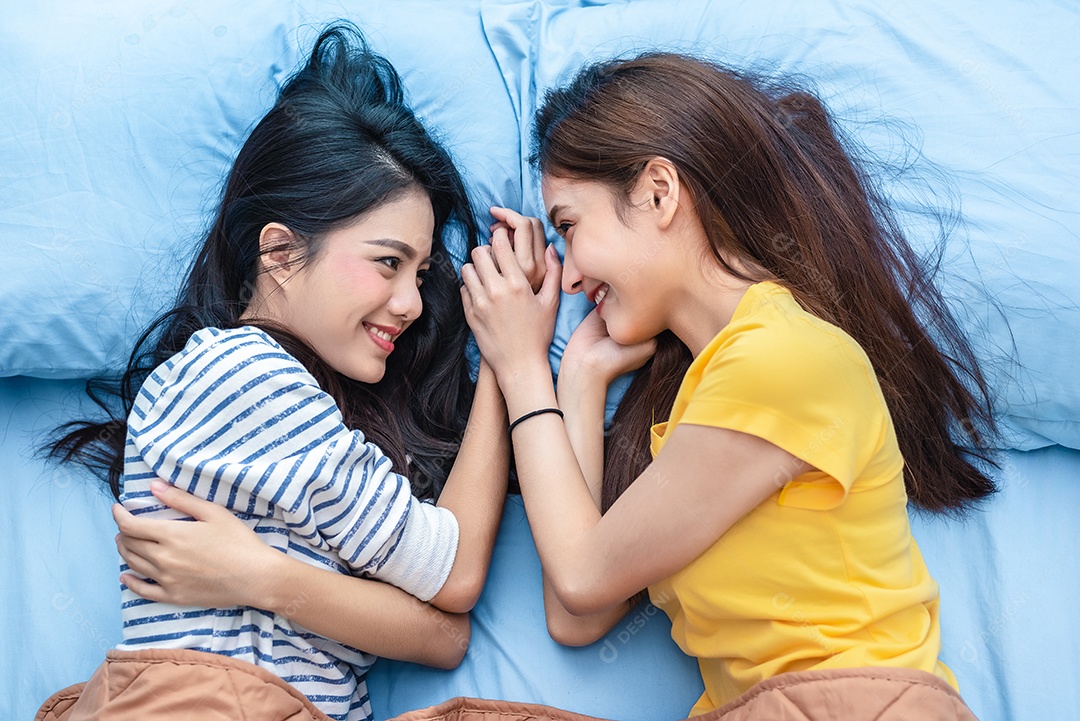 Duas mulheres asiáticas olhando uma para a outra quando deitadas na cama.