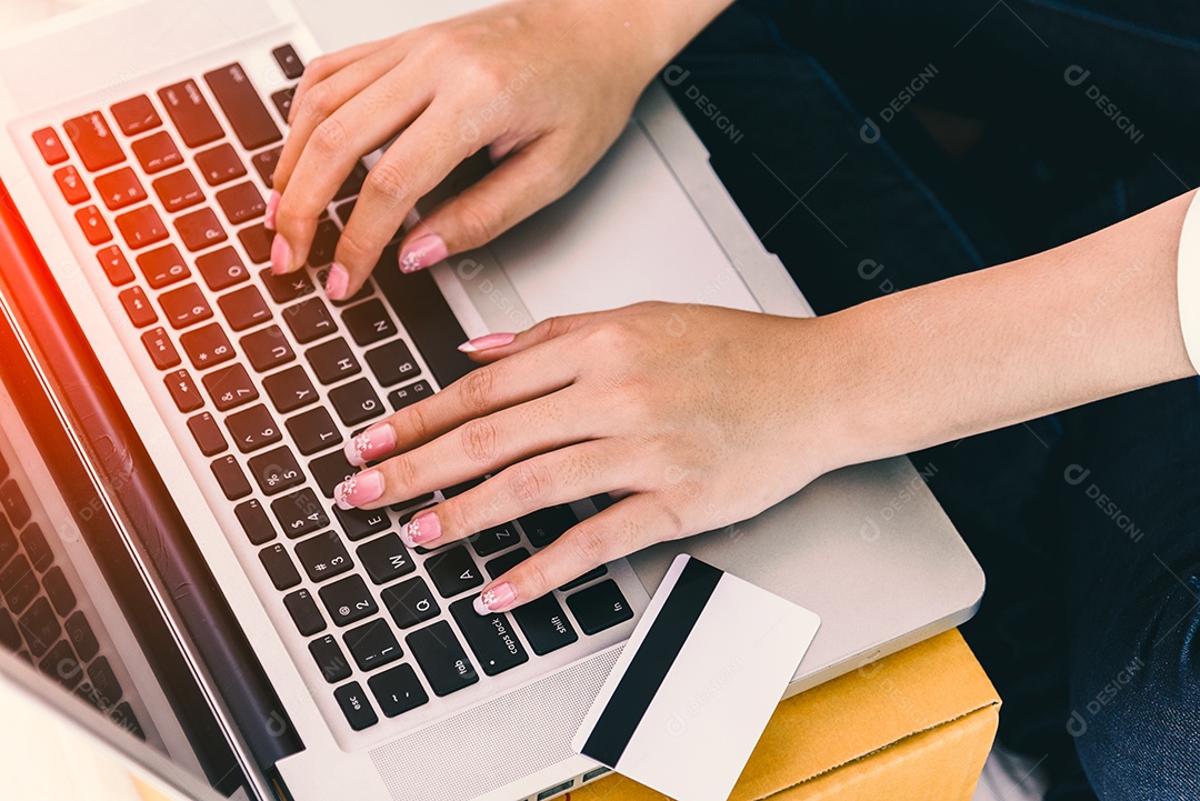 Feche as mãos da mulher usando o laptop com cartão de crédito ao lado.