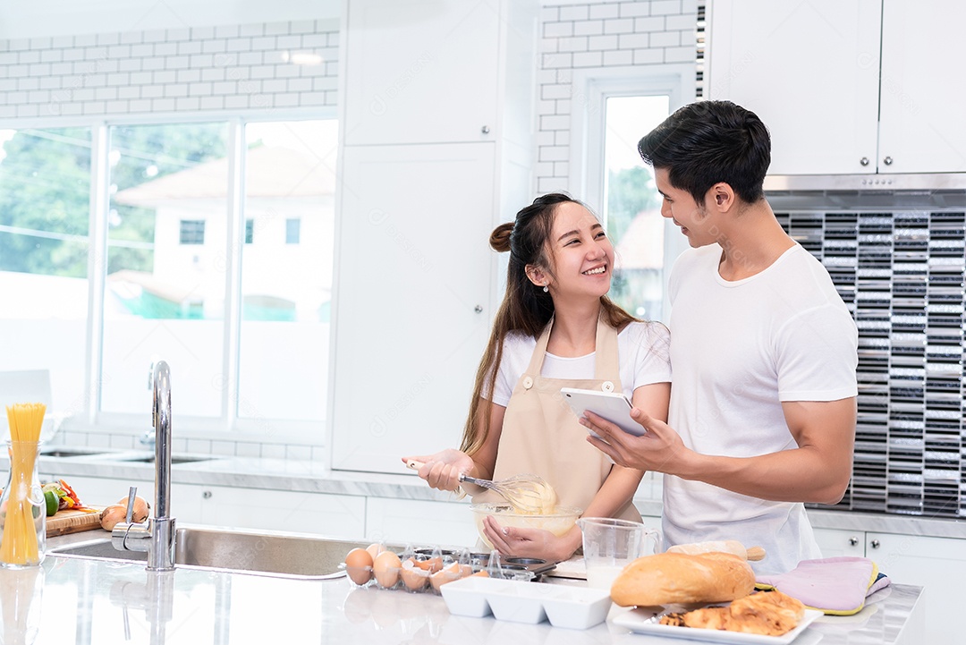 Casais asiáticos cozinhando e assando bolo juntos na cozinha em casa.
