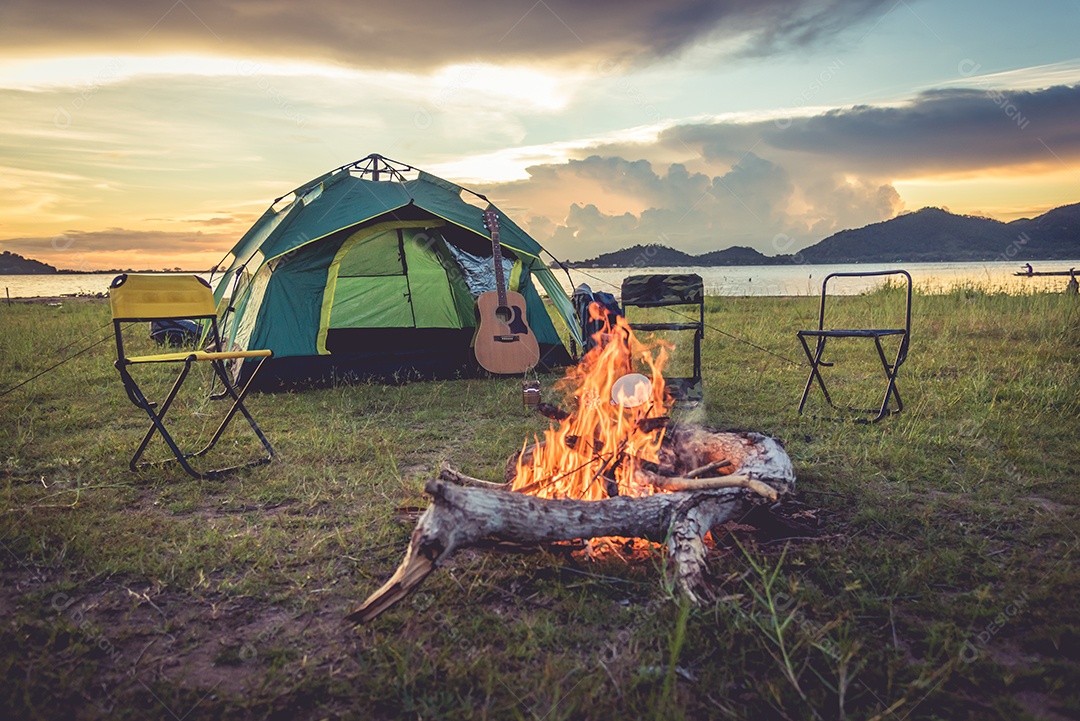 Barraca de acampamento com fogueira no campo verde prado, lago e fundo da montanha.