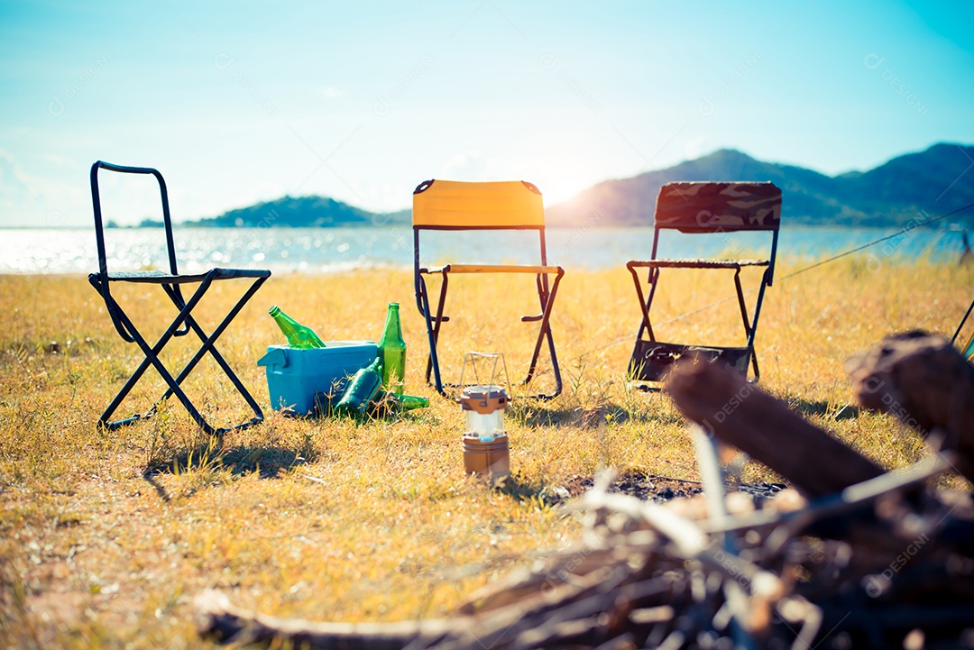 Três cadeiras de piquenique no campo Prado. Fogueira em primeiro plano e lago com montanha ao fundo.