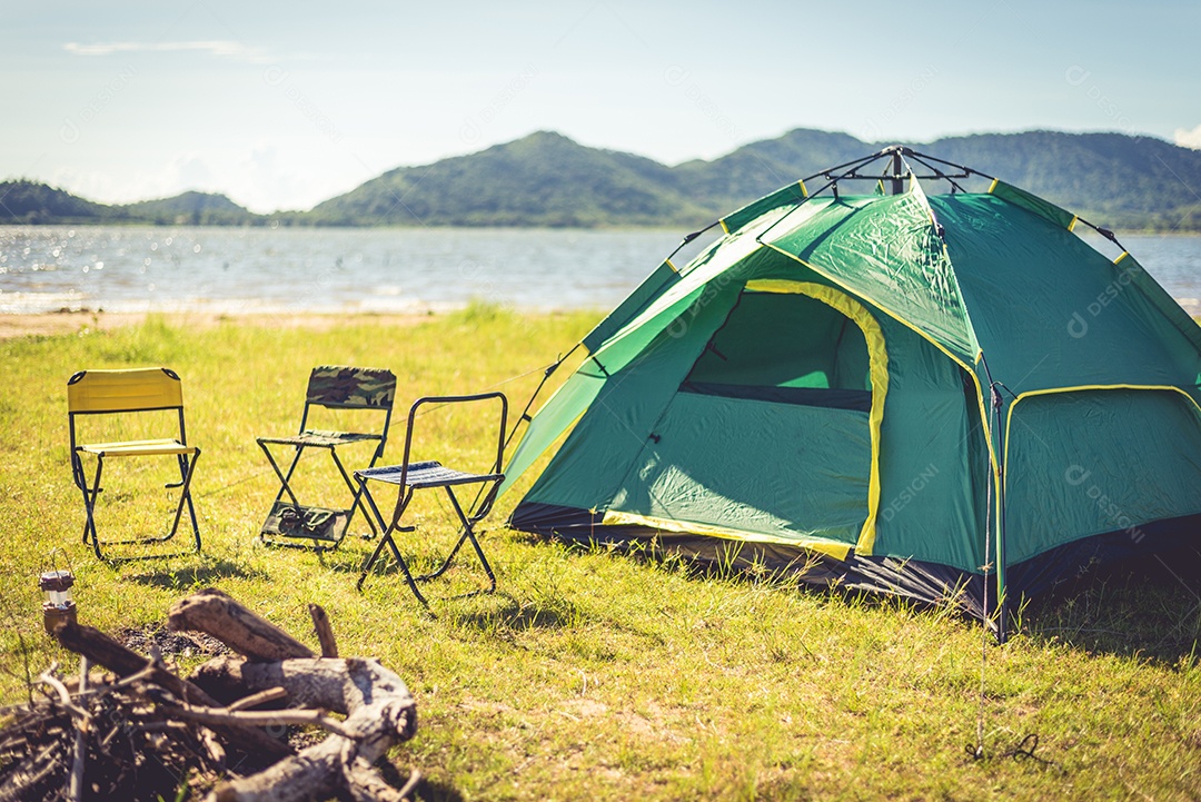 Barraca de acampamento com fogueira extinta no prado verde do campo, lago e fundo da montanha.