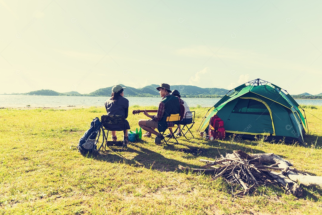 Grupo de viajantes acampando e fazendo piquenique e tocando música juntos. Fundo de montanha e lago.