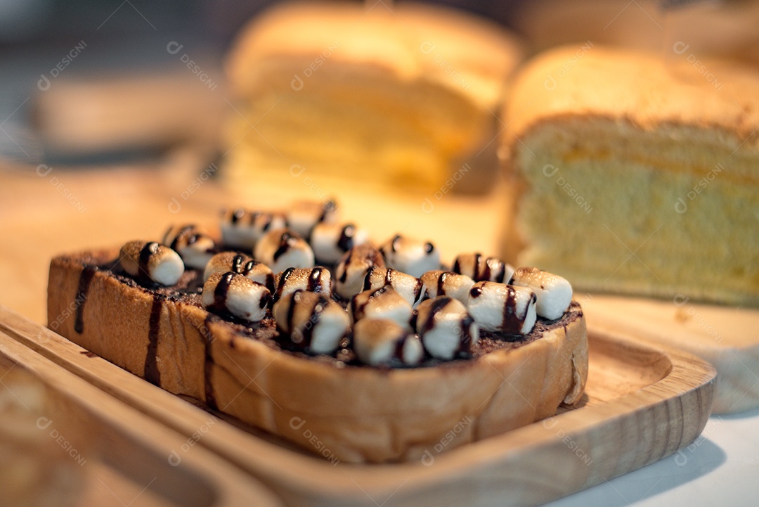 Pão torrado fatiado com cobertura de marshmello com calda de chocolate na placa de madeira.