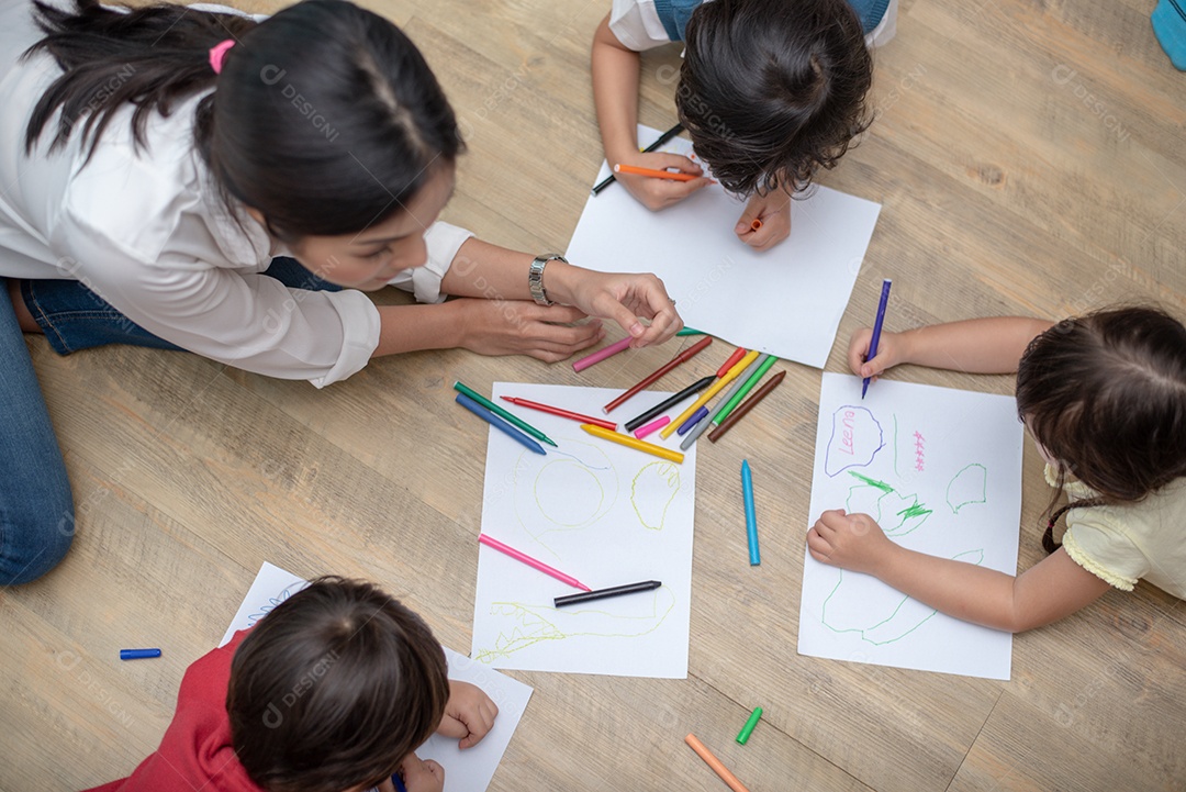 Grupo de alunos da pré-escola e professores desenhando em papel na aula de artes.