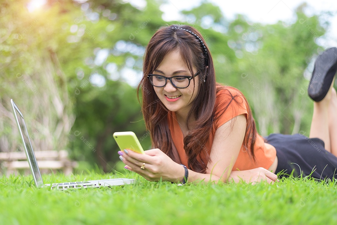 Mulher asiática feliz usando smartphone ao relaxar no parque. Conceito de pessoas e estilo de vida.