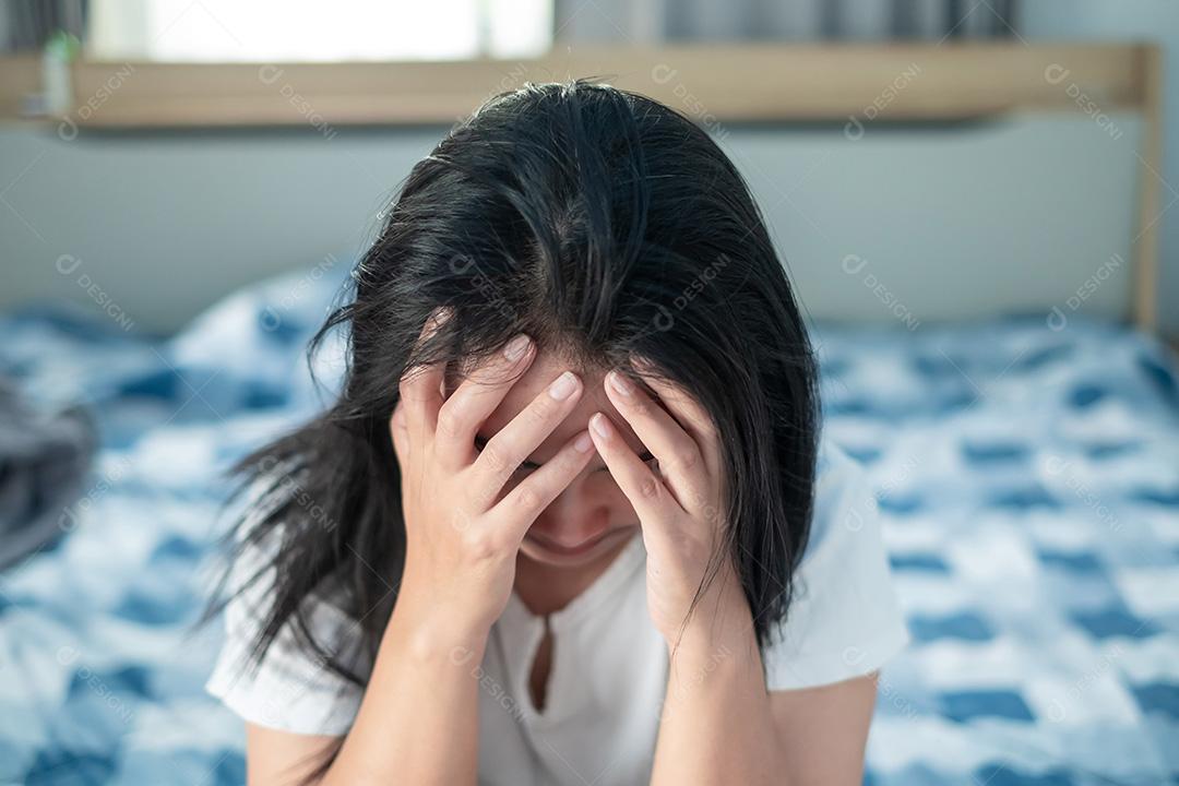 Mulher asiática na camisa branca sentada na cama segurando a cabeça expressando estresse, decepção, depressão, enxaquecas, problemas de saúde, cuidados de saúde e conceito de gerenciamento de estresse.