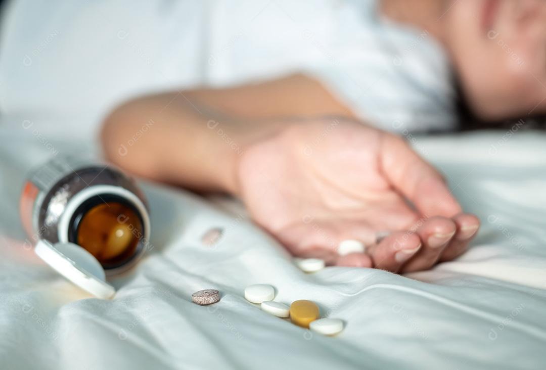 Mulher asiática de camisa branca está deitada inconsciente em uma cama branca após uma overdose de pílulas para perda de peso, selecione o foco nas pílulas para contar uma história