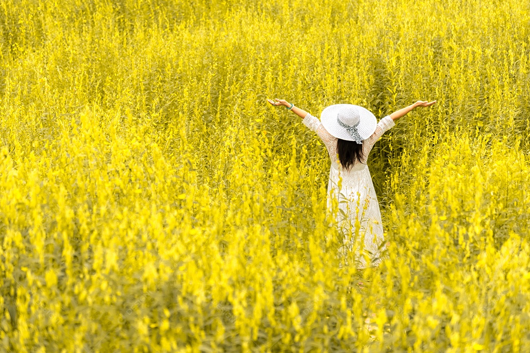 Vista traseira da mulher de beleza com chapéu de asa branca e vestido branco no prado de flores.