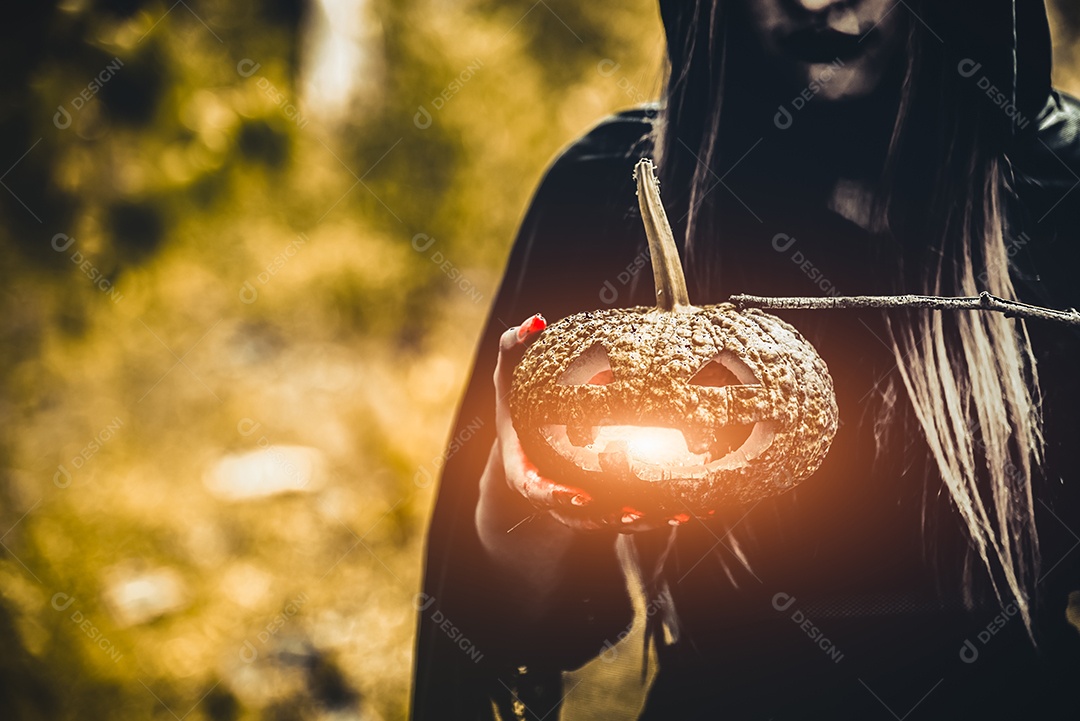Lanterna de abóbora na mão de bruxa. Mulher velha segurando abóbora na floresta verde escura.