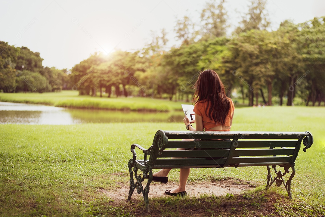 Vista traseira da mulher de beleza feliz em roupas casuais usando tablet no fundo do parque nacional.