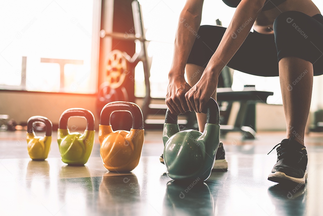 Close-up da mulher levantando kettlebell como halteres no centro de treinamento de ginásio de clube de esporte de fitness com equipamento de esporte perto do fundo da janela.