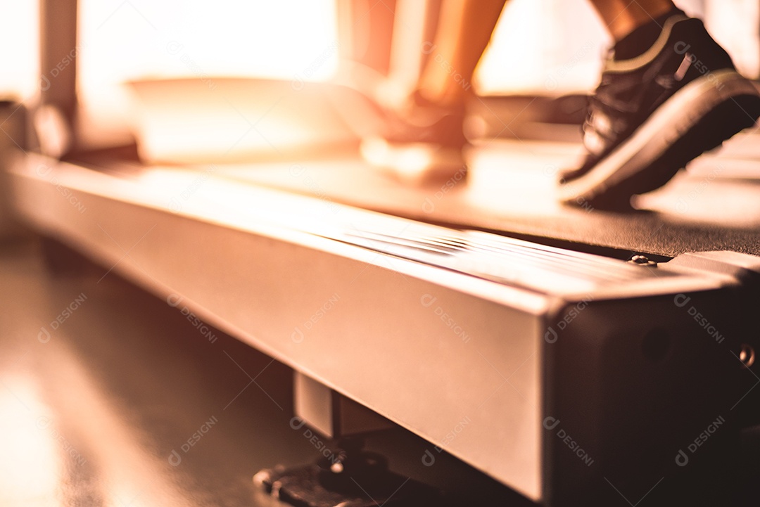 Feche de pernas de mulher correndo na esteira com roupas esportivas e tênis.