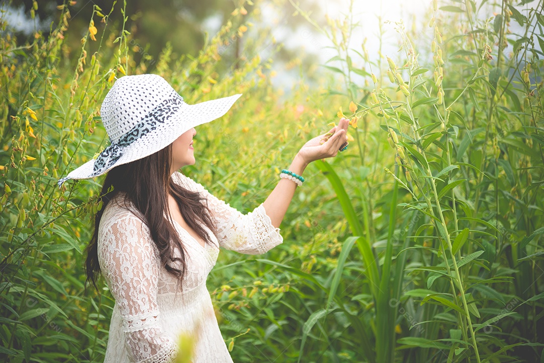 Mulher asiática de beleza em vestido branco e chapéu de asa andando em fundo de campo de flor de colza.