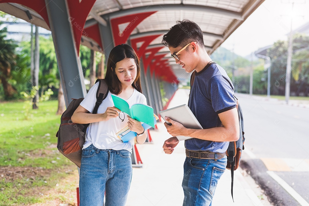 Dois jovens universitários asiáticos discutindo sobre a leitura de livros e o uso do laptop para pesquisar e aprender conhecimento.
