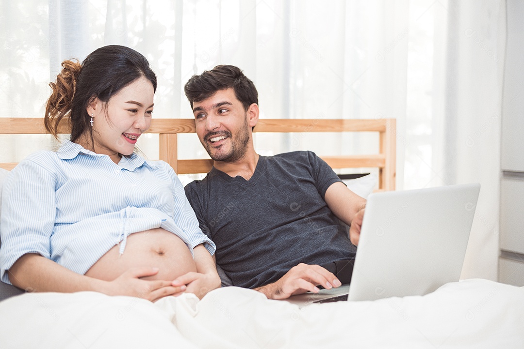 Homem feliz e sua esposa grávida usando laptop para pesquisar itens de bebê recém-nascido para preparar a paternidade.