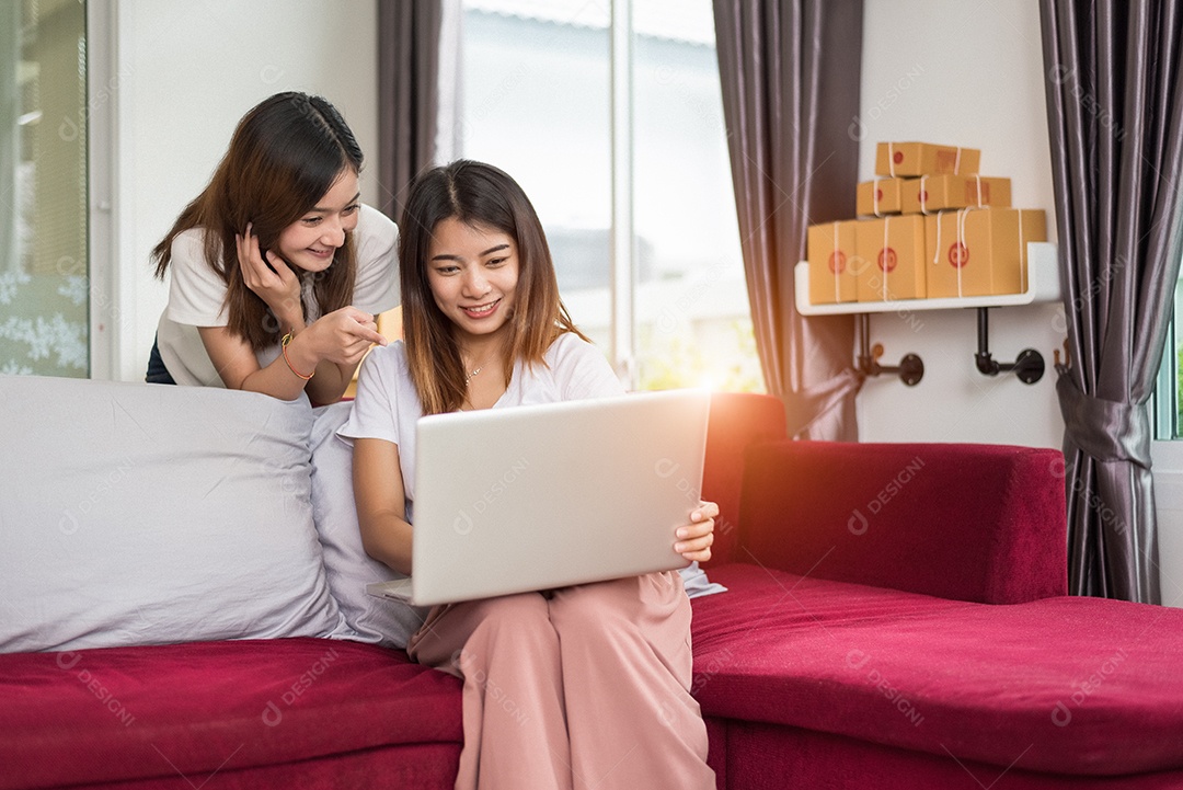 Duas jovens empresárias asiáticas freelancers trabalhando em casa no escritório com laptop sentado no sofá.