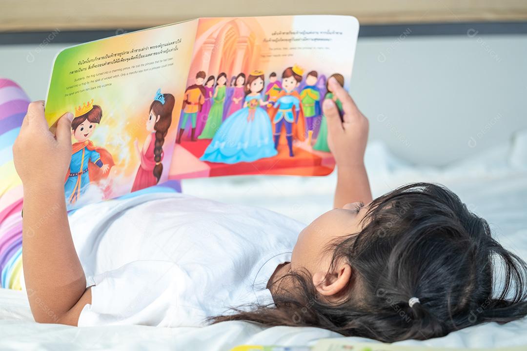 Menina asiática bonitinha lendo contos de fadas na cama branca no quarto, estudo, hobbies, lazer