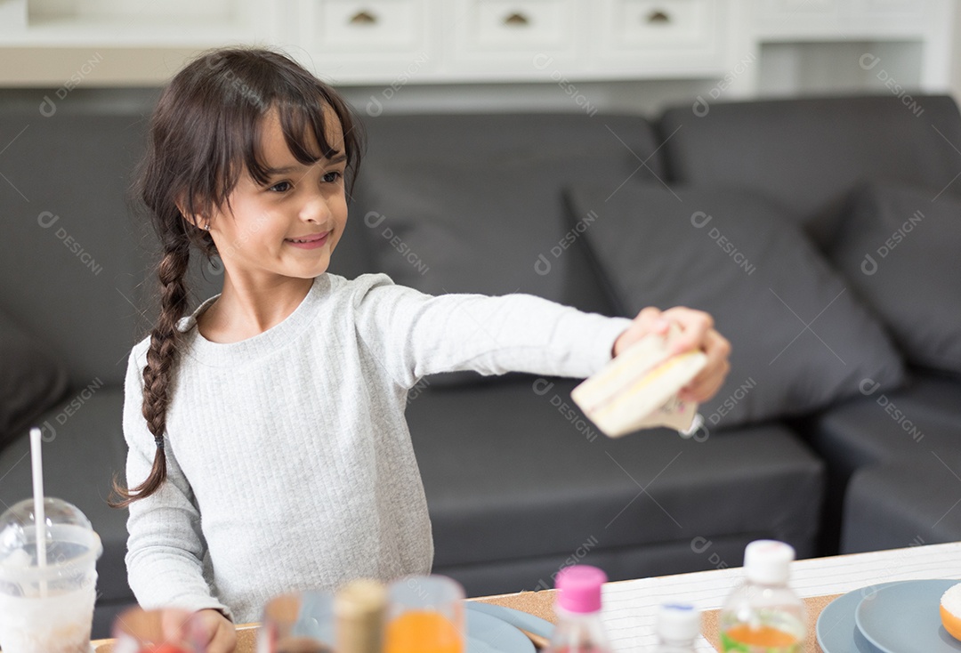 Menina feliz dando brinquedo de cozinhar sanduíche como chef na sala de estar.