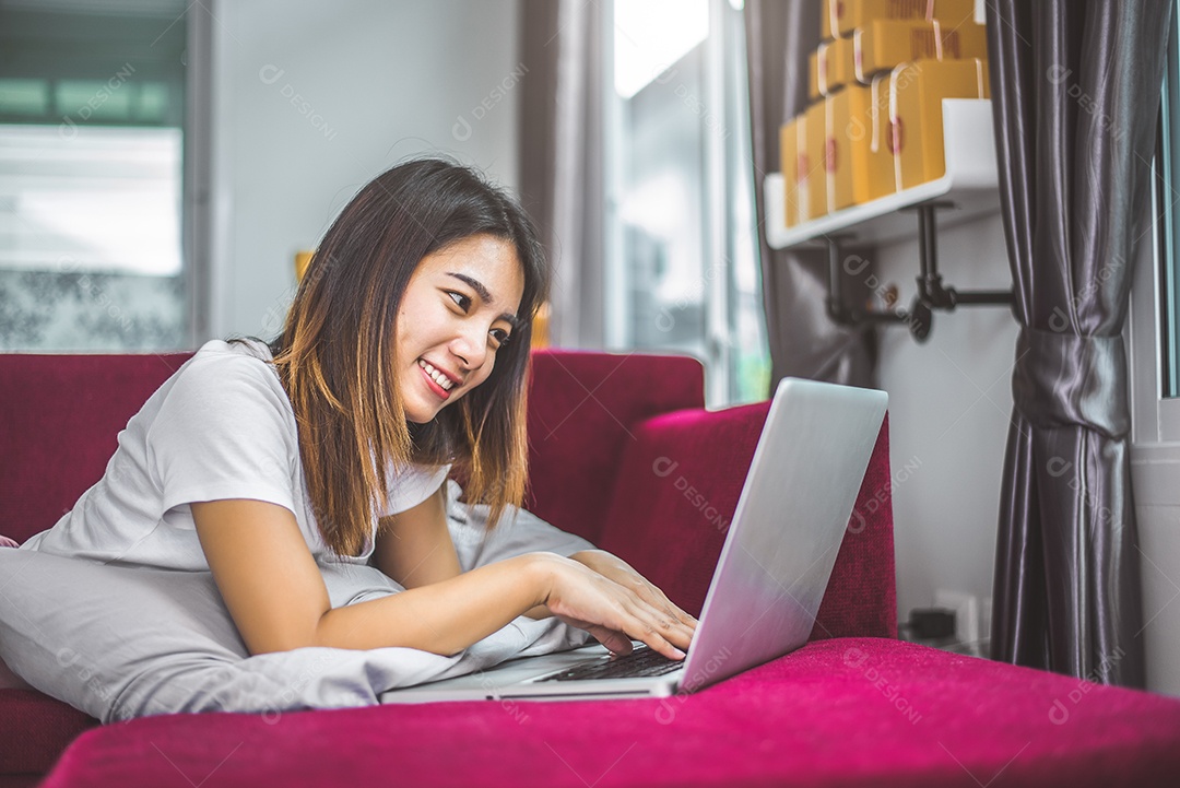 Jovem mulher navegando na internet pelo laptop no sofá vermelho.