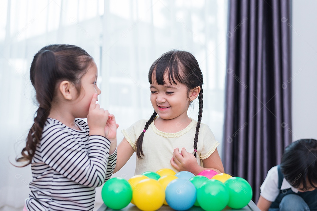 Duas meninas e um menino jogando pequenas bolas de brinquedo em casa juntos.