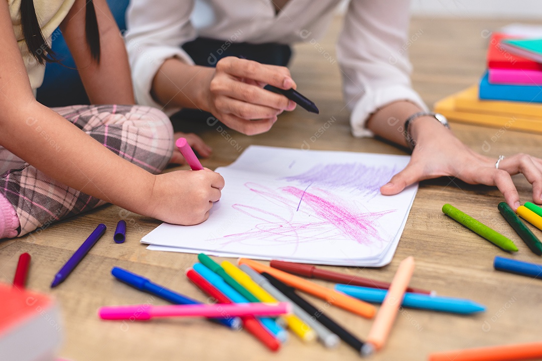 Mãos fechadas da mãe ensinando crianças a desenhar desenhos animados na aula de arte com caneta colorida.