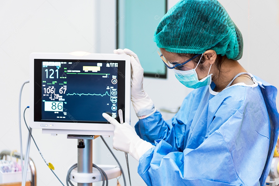 Médica apontando para monitor de frequência cardíaca na sala de operação.