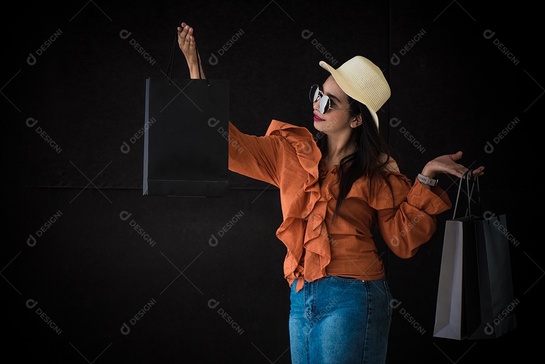 A mulher asiática da compra aprecia com o saco de compras de Black Friday no fundo preto.