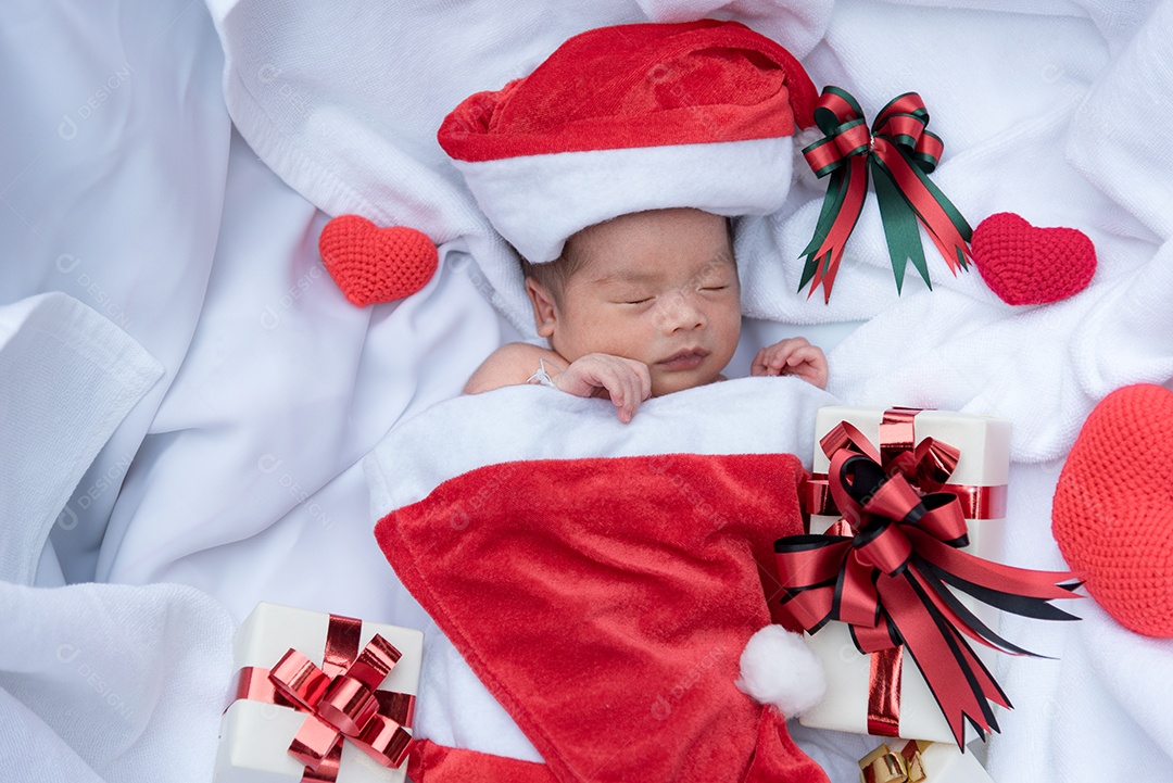 Rosto de bebê recém-nascido dormindo com chapéu de Natal com caixa de presente.