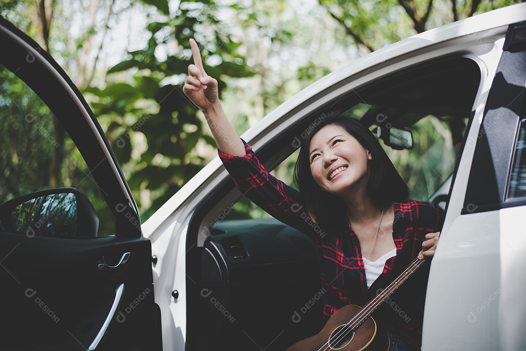 Mulher asiática de beleza apontando e se divertindo no verão ao ar livre com Ukulele no carro branco.