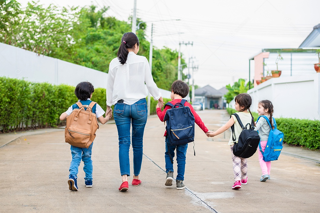 Grupo de alunos da pré-escola e professores de mãos dadas e caminhando.