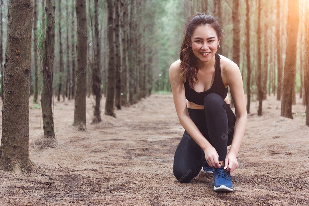 Mulher amarrando cadarços ao correr na floresta.