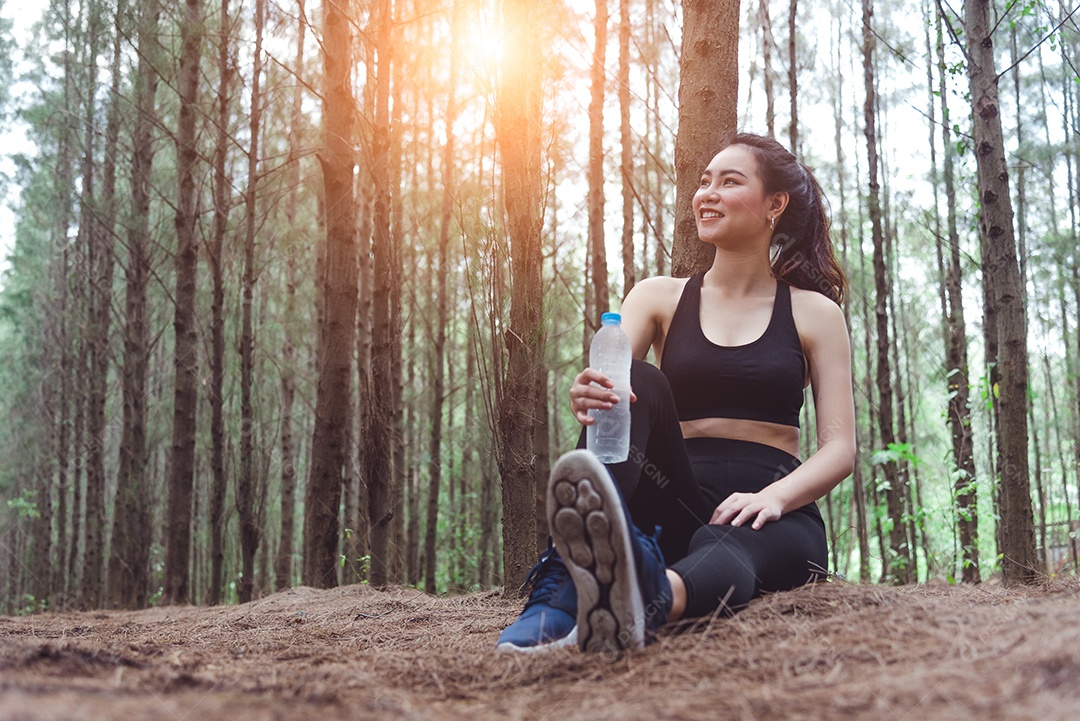 Mulher de esporte asiático de beleza descansando e segurando garrafa de água potável.