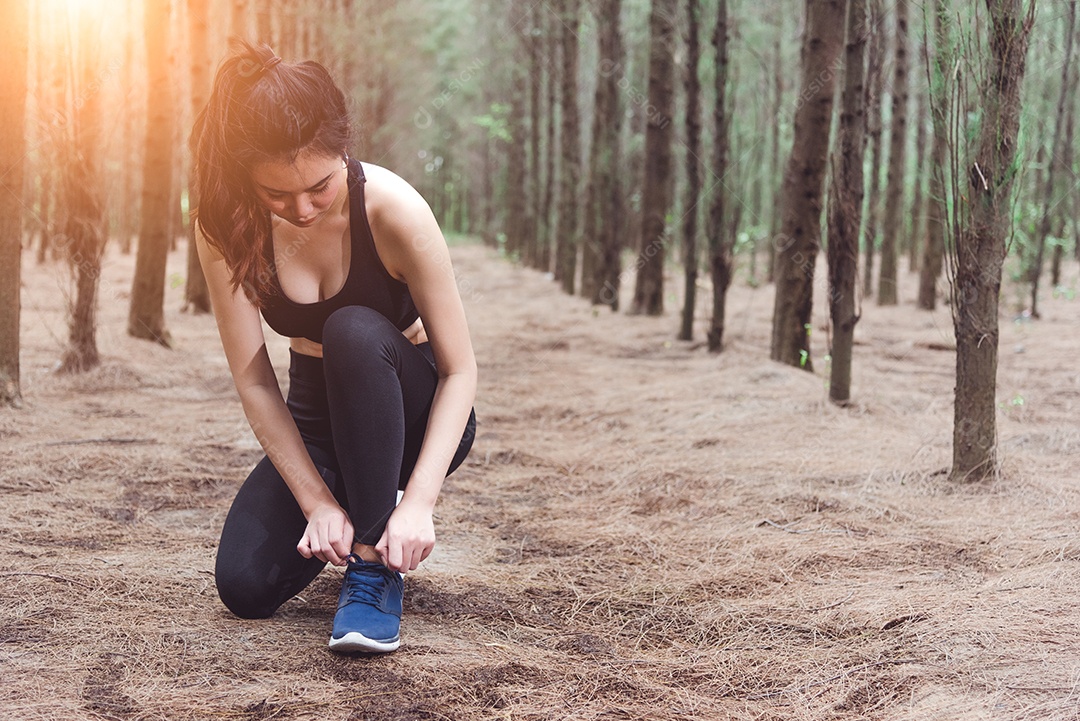 Mulher amarrando cadarços ao correr na floresta.