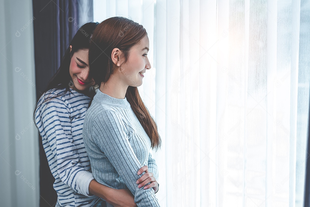 Two Asian lesbian women hug and cuddle together in bedroom.