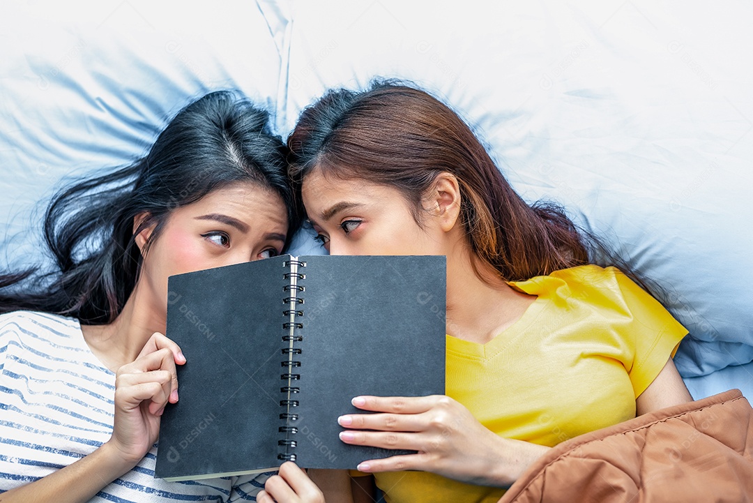 Lindo casal de lésbicas asiáticas lendo livro juntos e deitado na cama.