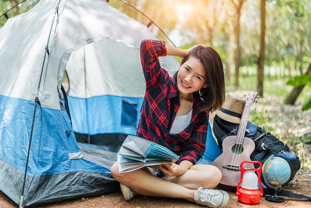Linda mulher asiática tocando Ukulele na frente da barraca de acampamento.