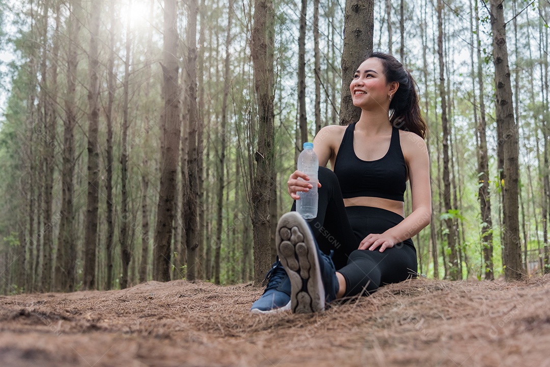 Mulher de esporte asiático de beleza descansando e segurando garrafa de água potável.