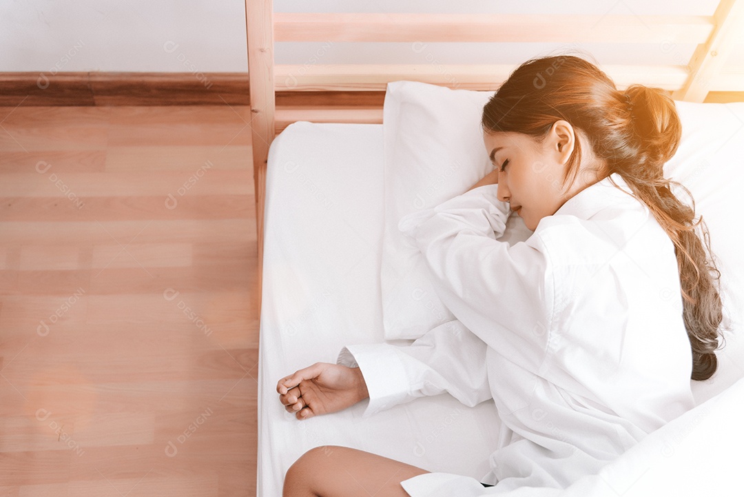 Jovem mulher asiática dormindo na cama branca pela manhã.