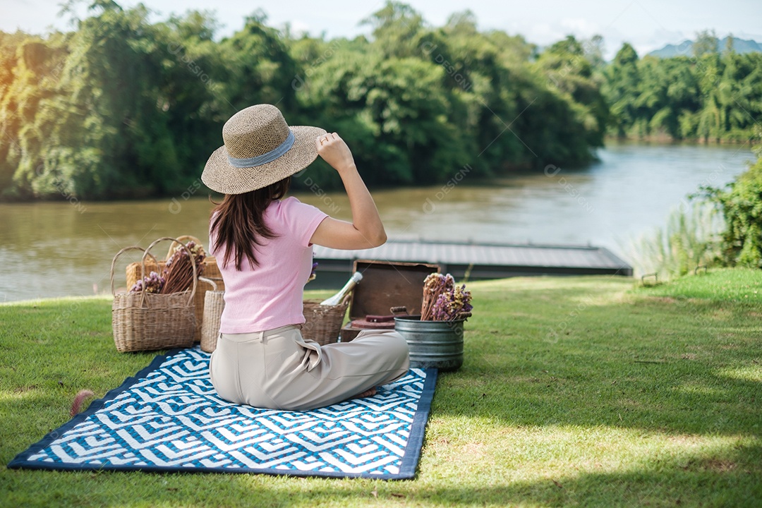 Mulher feliz com chapéu na hora do piquenique no parque perto do rio, verão, primavera e conceito de férias