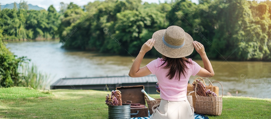 Mulher feliz com chapéu na hora do piquenique no parque perto do rio, verão, primavera e conceito de férias
