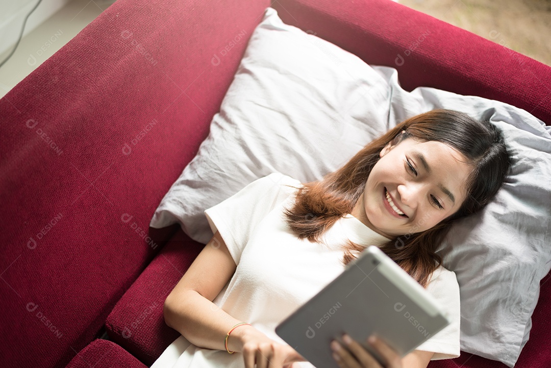 Mulher gosta de relaxar em casa com tablet no sofá vermelho. Relaxe e o conceito de férias.