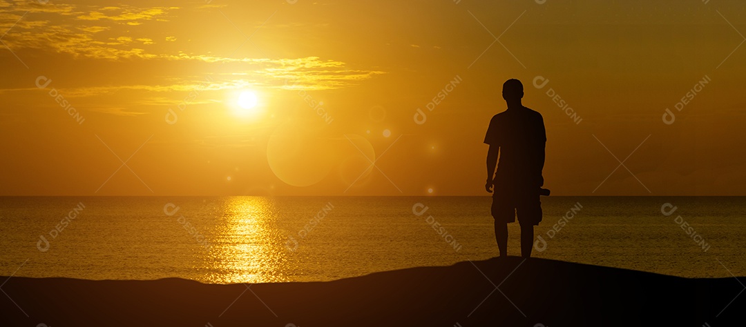 Uma visão panorâmica da silhueta de um homem segurando uma câmera olhando para um pôr do sol tranquilo sobre o oceano