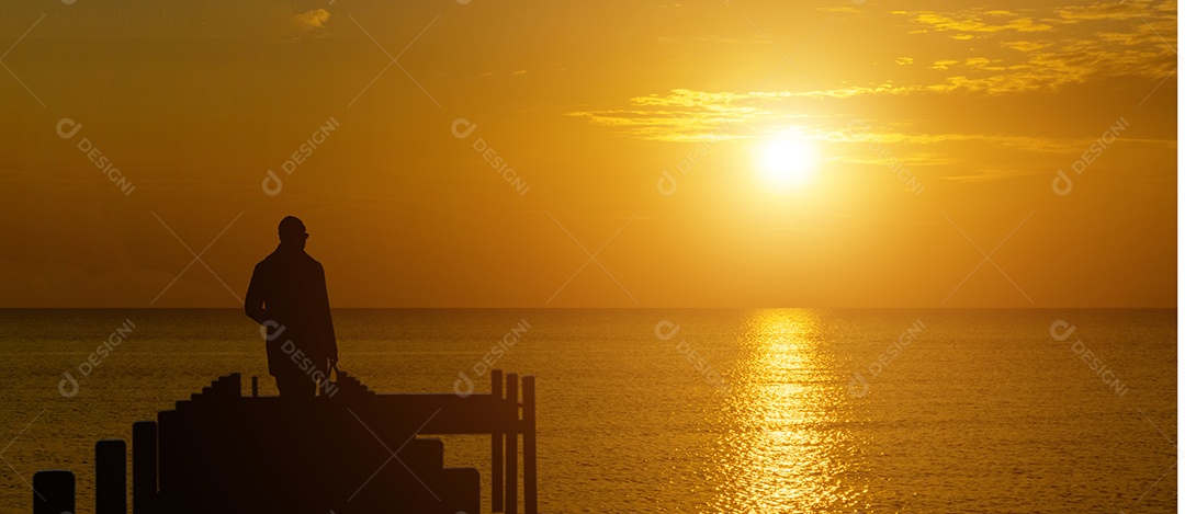 Visão panorâmica da silhueta de um homem olhando para um pôr do sol sereno sobre o oceano