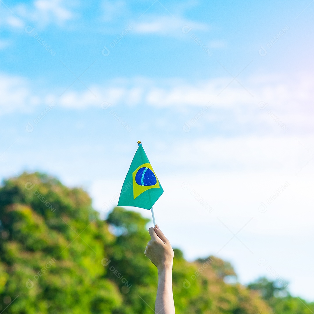 mão segurando a bandeira do Brasil sobre fundo de céu azul. Dia da independência de setembro e conceitos de celebração feliz