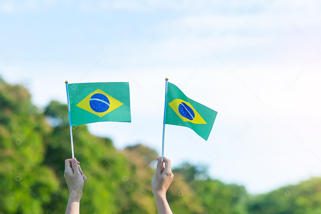 mão segurando a bandeira do Brasil sobre fundo de céu azul. Dia da independência de setembro e conceitos de celebração feliz